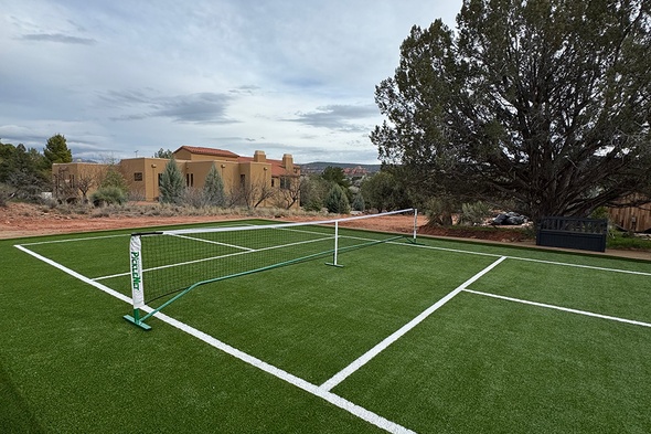 Completed synthetic grass installation pickleball court with regulation net and crisp white boundary lines set against a stunning Sedona, Arizona backdrop of red rock cliffs, desert shrubs, and a Southwestern-style home.