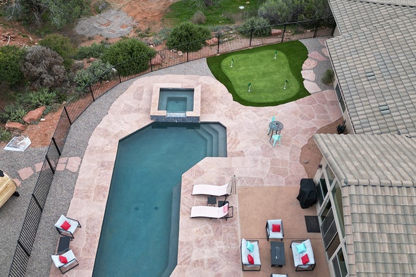 Aerial view of a complete backyard transformation featuring a synthetic grass installation putting green with cup flags seamlessly integrated alongside a geometric pool, spa, and expansive stamped concrete patio in Sedona, Arizona.
